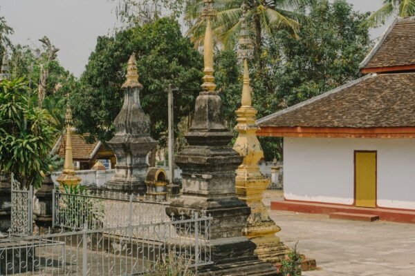 A white and yellow temple building beside trees in Luang Prabang