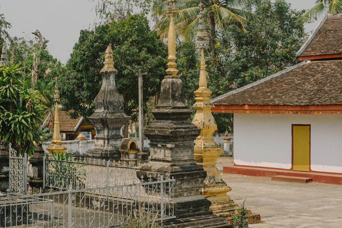 A white and yellow temple building beside trees in Luang Prabang