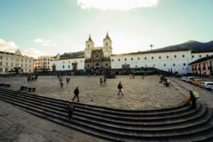 People crossing a broad square before a white church in Quito