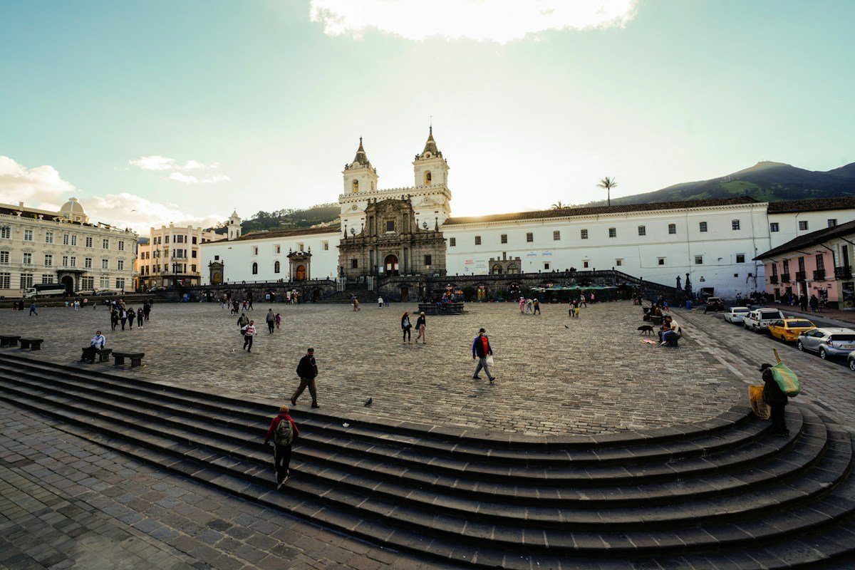 People crossing a broad square before a white church in Quito